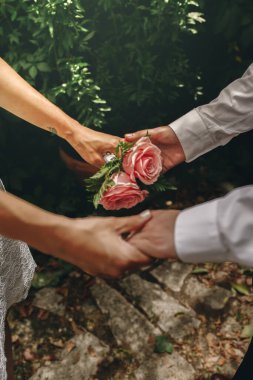 Yeni evlilerin elleri birbirine kenetlenmiştir. Gül buketine odaklan. Birlik ve aşk kavramı.