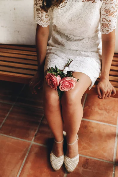 เจ้าสาวในชุดแต่งงานสั้นและช่อดอกกุหลาบสีชมพูน้อยของเธอนั่งและรอในม้านั่งไม้ คอนเซปต์วันแต่งงาน . — ภาพถ่ายสต็อก