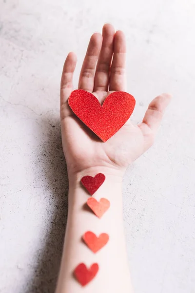 Kırmızı parıltılı kalp ellerinde karton, beyaz arka planda küçük kalpler. Aşk ve Sevgililer Günü kavramı. — Stok fotoğraf