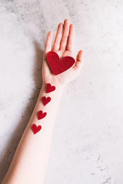 กระดาษแข็งรูปหัวใจสีแดงแวววาวบนมือและหัวใจเล็ก ๆ บนพื้นหลังสีขาว แนวคิดของความรักและวันวาเลนไทน์ . — ภาพถ่ายสต็อก
