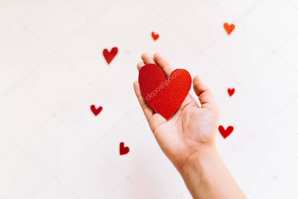 Red glitter heart shaped cardboard on the hand and small hearts on white background. Love and valentines day concept.