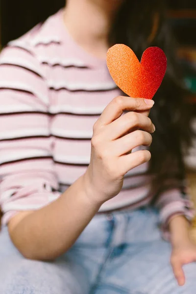ผู้หญิงสาวที่มีกระดาษแข็งรูปหัวใจแวววาวสีแดงบนมือ ผู้หญิงที่ถือหัวใจกระดาษแข็งสําหรับวันวาเลนไทน์ ความรักและวันวาเลนไทน์ . — ภาพถ่ายสต็อก