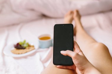 Genç bir kadın evinde kahvaltı yapıyor, cep telefonunu kontrol ediyor. Cep telefonuna odaklan..