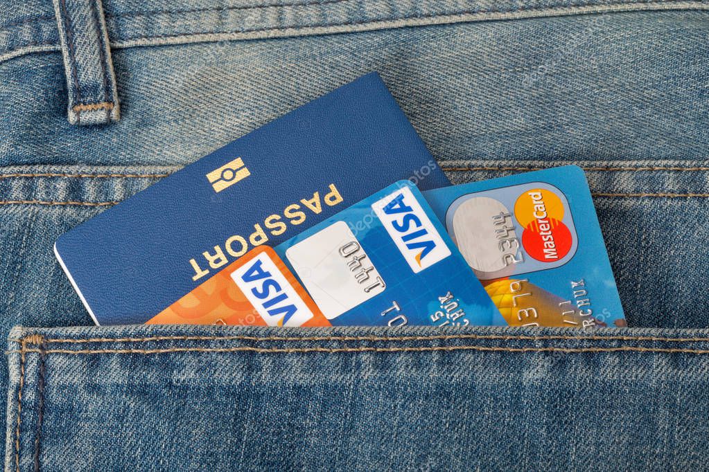 KIEV, UKRAINE - AUGUST 09, 2016: Blue biometric passport with three credit cards, Visa and MasterCard, in back pocket of blue jeans closeup.