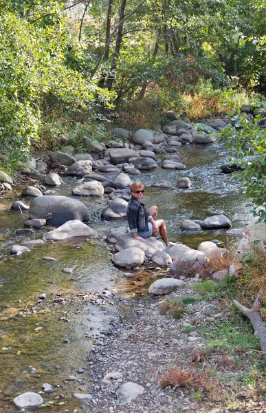Sonbaharda dağ nehir kaya üzerinde oturan kadın
