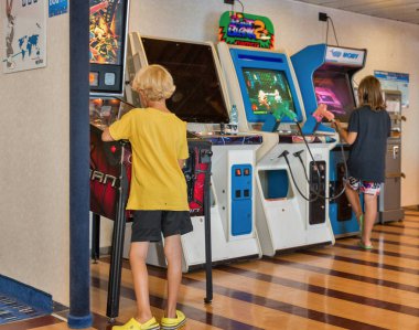 Çocuklar atari makinesinde dövüş oyunu oynarlar. Moby feribot gemisi.