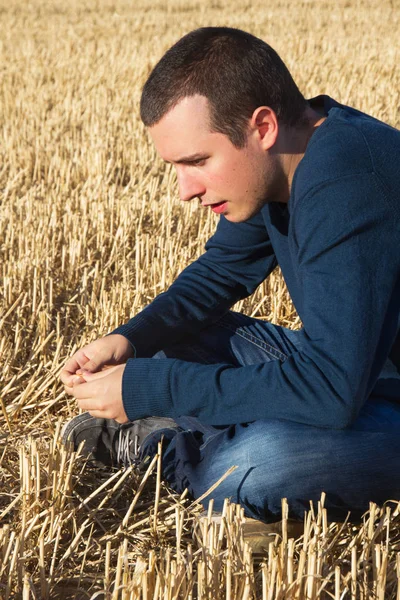 Pensiero profilo giovane seduto su un campo di cereali falciato — Foto Stock