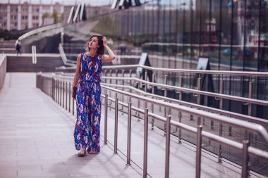 Parlak elbiseli genç bir kadın şehir parkında yürüyor ve yaz gününün tadını çıkarıyor.