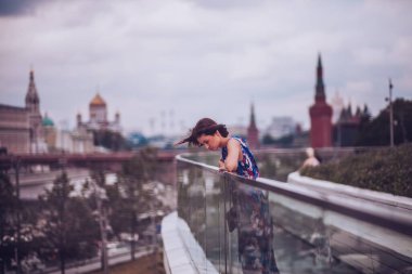 Parlak elbiseli genç bir kadın şehir parkında yürüyor ve yaz gününün tadını çıkarıyor.