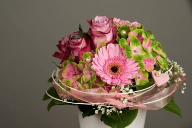 Beyaz vazoda gül ve gerberalar bulunan güzel çiçek buketi, sade bir arka planda.