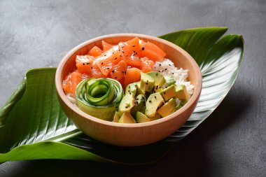Avokado, salatalık, pirinç ve susam tohumlu Hawaii Somon Kabı tropikal yaprakların üzerinde servis edilir. Suşi kasesi. Organik ve sağlıklı yiyecekler. Taze deniz ürünleri tarifi