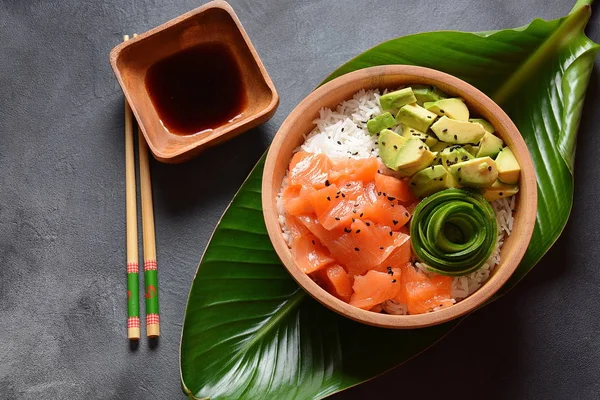 Hawaiian Salmon Poke Bowl with avocado, cucumber , rice and sesame seeds served in bowl on tropical leaves. Sushi bowl.Organic and healthy food. Fresh seafood recipe