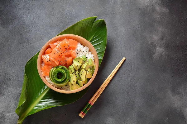 Hawaiian Salmon Poke Bowl with avocado, cucumber , rice and sesame seeds served in bowl on tropical leaves. Sushi bowl.Organic and healthy food. Fresh seafood recipe