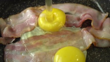 Tavaya koyulan ikinci tavuk yumurtası. Tavada yumurta ile kızartılmış iki dilim pastırma. Yaklaş. Makro. Yağlı ve renkli kızarmış domuz pastırması, sıcak bir tavada cızırtı ve sigara..