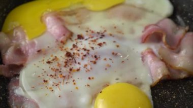İki dilim pastırma, tavada kızartılmış baharatlı iki yumurta. Tavada yumurta ile kızartılmış iki dilim pastırma. Yaklaş. Makro. Yağlı ve renkli kızarmış domuz pastırması, sıcak bir tavada cızırtı ve sigara..