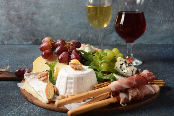 Appetizers table with snacks. Antipasto Cheese Board, salami and prosciutto crudo with grissini bread sticks served with glasses of wine. Traditional French, Spanish or Italian food concept