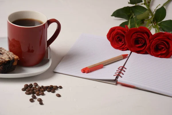 Cup of coffee, notebook, pen and rose flowers. Morning coffee break