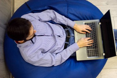 Serbest çalışan bir iş adamı. Genç yakışıklı adam dizüstü bilgisayarda çalışıyor ve mavi armut çantasının üzerinde oturuyor.