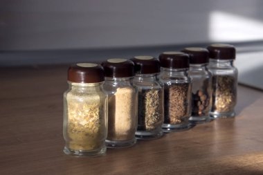 Bir sıra baharat kavanozu içinde çeşitli otlar ve baharatlar var.