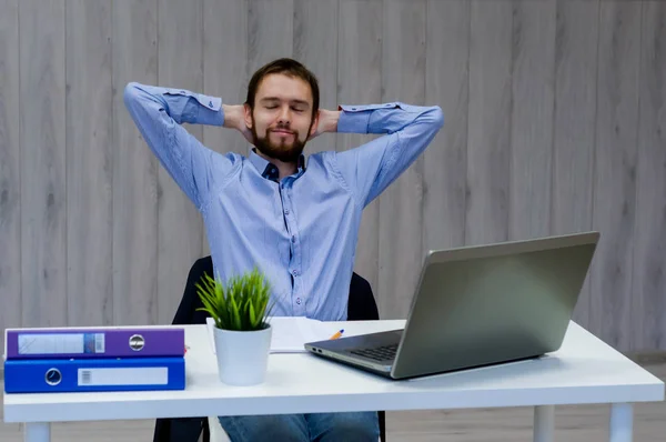 Tomando tiempo para un descanso minuto. Joven alegre sosteniendo las manos detrás de la cabeza y manteniendo los ojos cerrados mientras está sentado en su lugar de trabajo — Foto de Stock