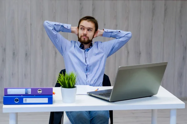 Tomando tiempo para un descanso minuto. Joven alegre sosteniendo las manos detrás de la cabeza y manteniendo los ojos cerrados mientras está sentado en su lugar de trabajo — Foto de Stock