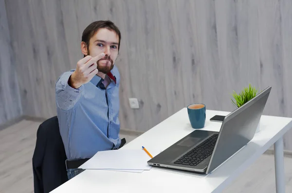 Портрет рассерженной бородатой бородатой молодой большой босс в синих джинсах рубашка сидит в офисе, работает с ноутбуком и показывает ебать — стоковое фото