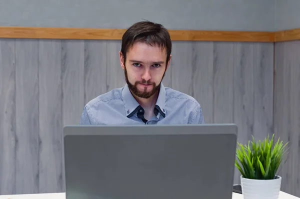 Joven hombre de negocios vestido con camisa azul mientras usa el ordenador portátil en la oficina . —  Fotos de Stock