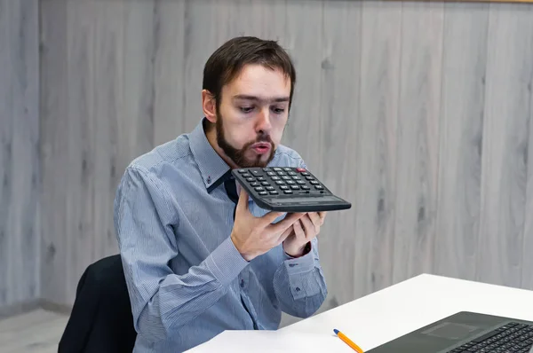 the man in the office blows dust off a calculator that he has not used for a long time