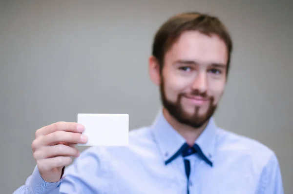Joven hombre de negocios sosteniendo la tarjeta de visita blanca en el fondo borroso oficina moderna —  Fotos de Stock
