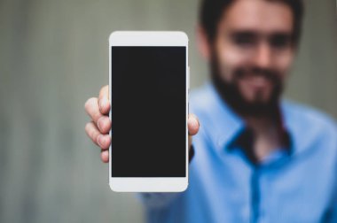 İş adamı cep telefonunu tutar ve gösterir. Takım elbiseli sakallı adam boş ekranlı akıllı telefon gösteriyor. İş, iletişim, internet, teknoloji kavramı