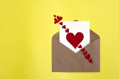 Beyaz kart el işi zarfında kırmızı kağıt kalpler ve sarı arka planda Cupids oku.