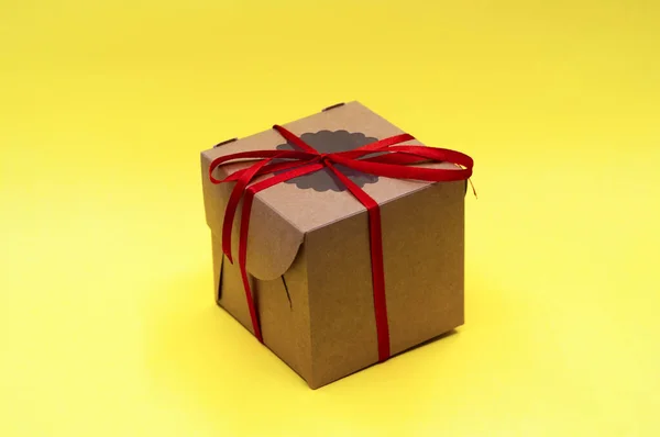 Bruine ambachtelijke geschenkdoos met rood lint strik op gele achtergrond — Stockfoto