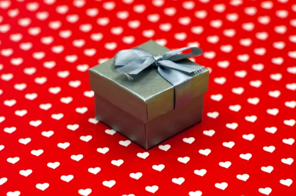 Kleine grijze geschenkdoos op witte en rode hartjes achtergrond. Valentijnsdag, huwelijk, liefde, geluk concept — Stockfoto