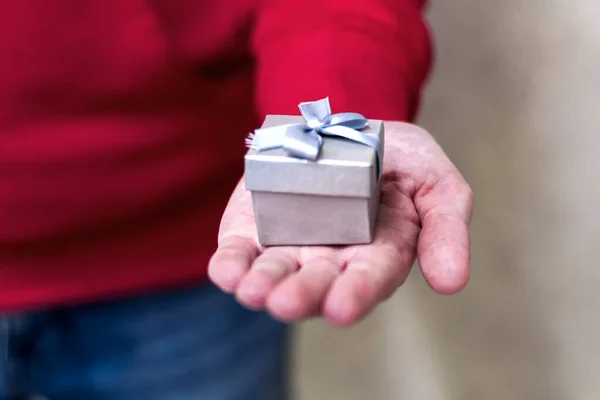 Close-up em mãos homem dando uma pequena caixa de presente cinza — Fotografia de Stock