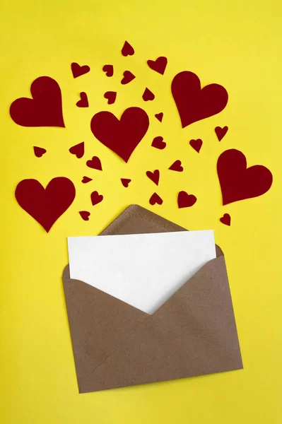 Червоні паперові серця вилітають з конверта ремісничого паперу на жовтому тлі. День святого Валентина. любовна концепція. Подарунок, повідомлення для коханця. Простір для тексту. Квадратний банер — стокове фото