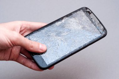 Kırık ekran gri arka plan üzerinde el ile Smartphone.