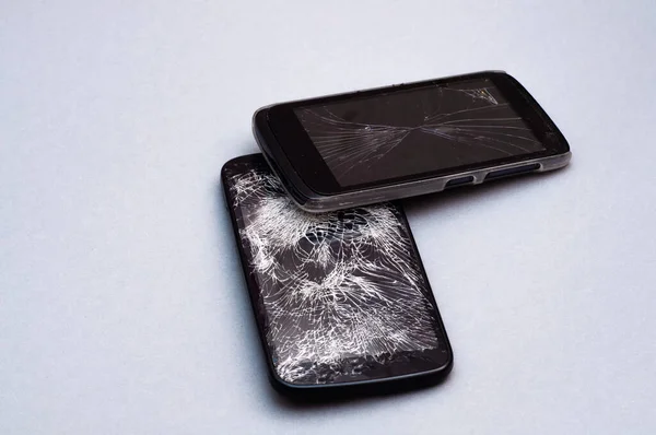 Dos teléfonos inteligentes con pantalla rota sobre fondo gris . — Foto de Stock