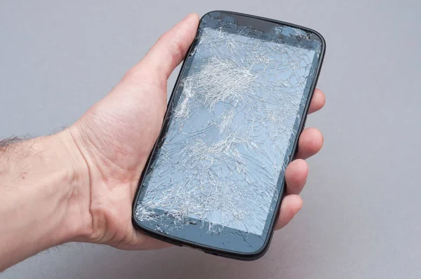 Smartphone with broken screen in hand on grey background.
