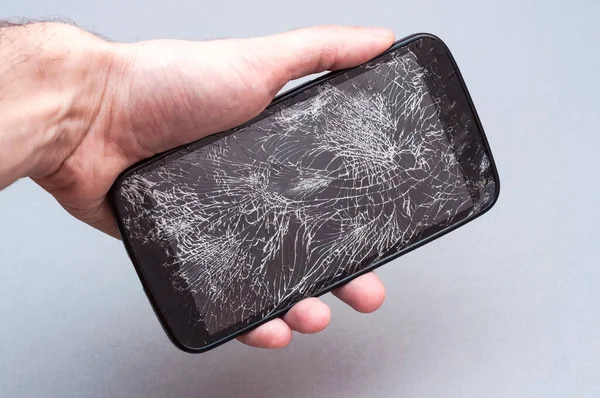 Smartphone con pantalla rota en la mano sobre fondo gris . — Foto de Stock