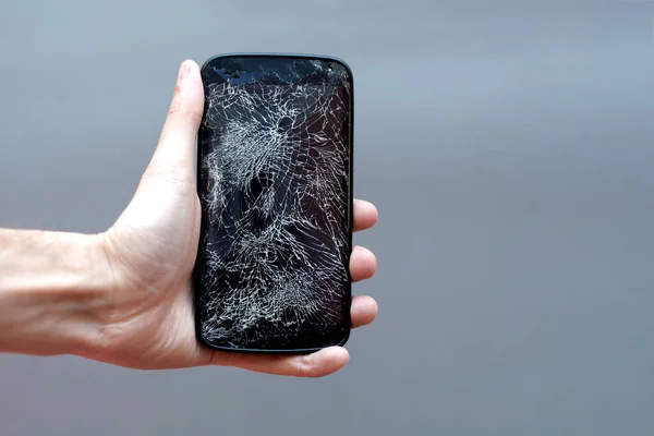Smartphone with broken screen in hand on grey background.