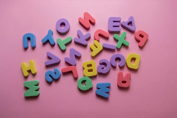 Colorful plastic alphabet letters on pink background, top view