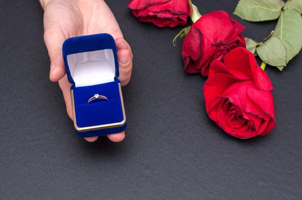 Bröllop ring i rutan i handen med röda rosor blomma på svart bakgrund. — Stockfoto
