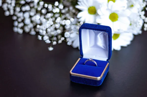 Förlovning diamantring i blå presentförpackning på hög med vita blommor kronblad. Symbol för kärlek och äktenskap. — Stockfoto