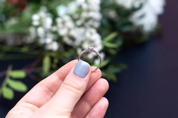 검은 배경에 흰 꽃이 달린우아 한 다이아몬드 반지를 들고 있는 여인의 손을 꼭 잡고 있는 모습. — 스톡 사진