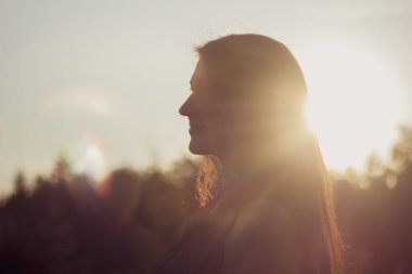 Güneşin batışında güzel bir kadının yakın plan portresi. Sıcak ve güneş ışığının tadını çıkarıyor.
