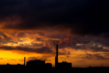 Gün batımında şehrin birkaç blok ötesinde elektrik santrali emisyonları görülüyor. Çevre kirliliği. Fabrika borusu havayı kirletiyor.