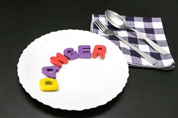 Colorful letters with word danger on plate with fork and knife, food additive and unhealthy food concept.
