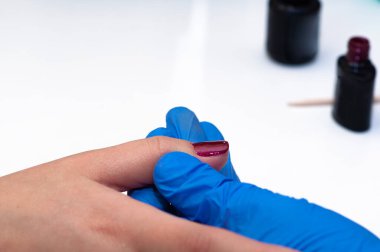 Manikür uzmanı, güzellik salonundaki sağlıklı doğal kadın tırnaklarına kırmızı oje sürüyor.