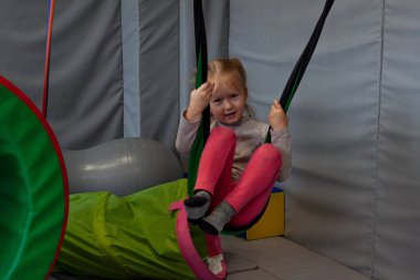 Fizyoterapisti ona yardım ederken hamakta duyusal terapinin tadını çıkaran tatlı küçük bir kız.