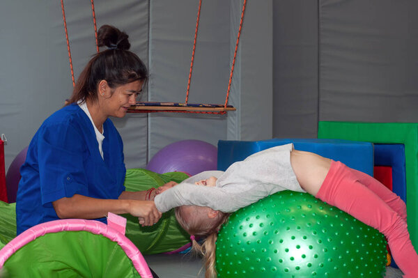 сенсорный терапевт массирует маленькую девочку большим мячом
